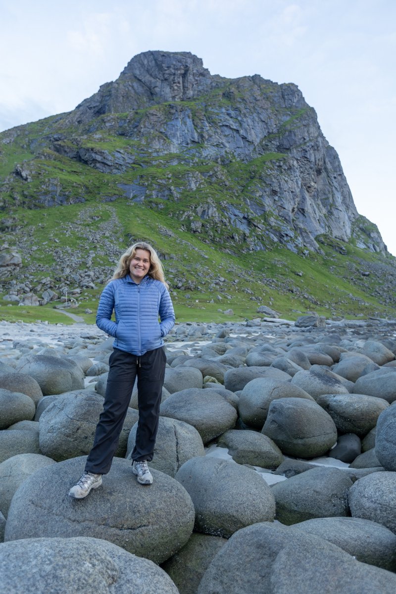Woman standing on a rocky shoreline below a mountain